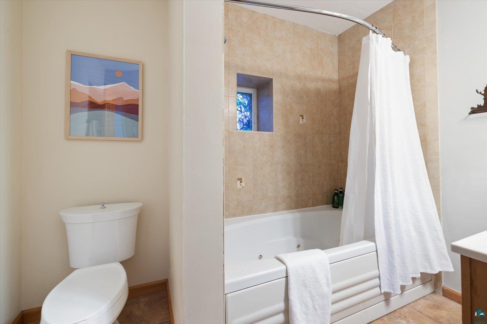 6266 Giants Ridge Road Biwabik, MN 55705 - Photo 31 of 37 Tiled bath enclosure featuring a white tub, curved shower rod, and built-in wall niche with stained glass