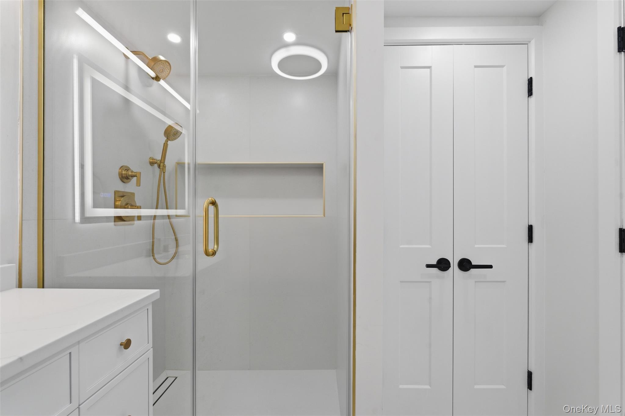 40 Calhoun Avenue New Rochelle, NY 10801 - Photo 33 of 49 Modern bathroom featuring a glass-enclosed shower with gold-tone fixtures, a built-in shower niche, and a contrasting white vanity with coordinating hardware