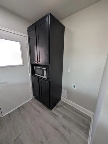 a view of an empty room with wooden floor and kitchen view