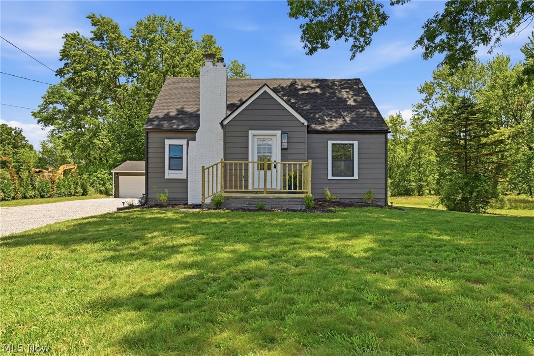 951 Bey Road Akron, OH 44312 - Photo 2 of 34 Charming gray siding residence featuring a white brick chimney, front porch with natural wood railings, and a gravel driveway leading to an attached garage