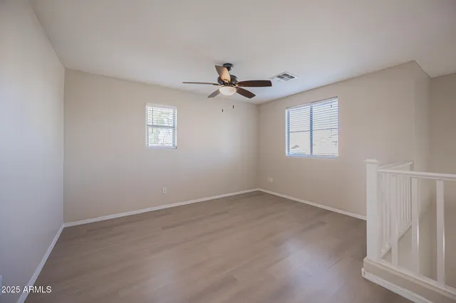an empty room with wooden floor ceiling fan and windows