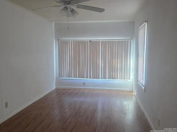 an empty room with wooden floor fan and windows