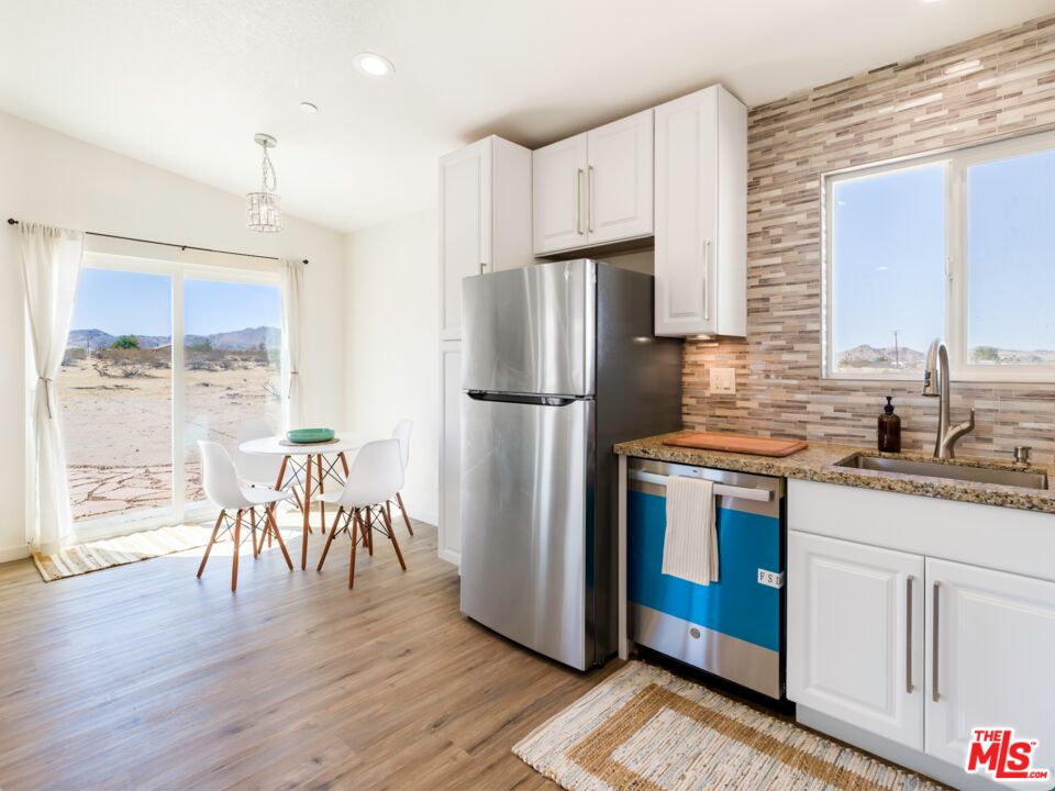 63618 2 Mile Road Joshua Tree, CA 92252 - Photo 7 of 28 a kitchen with granite countertop a refrigerator a stove a sink a dining table and chairs with wooden floor
