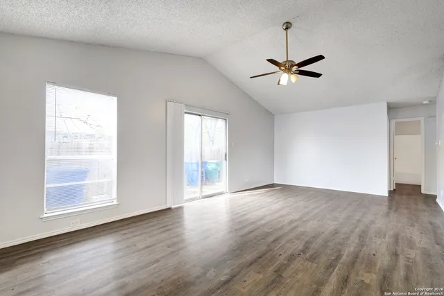 an empty room with wooden floor ceiling fan and windows