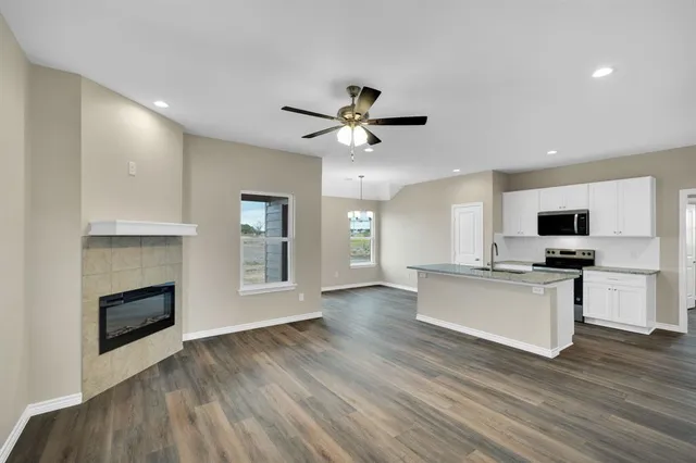 a living room with stainless steel appliances kitchen island a fireplace wooden floor and a ceiling fan