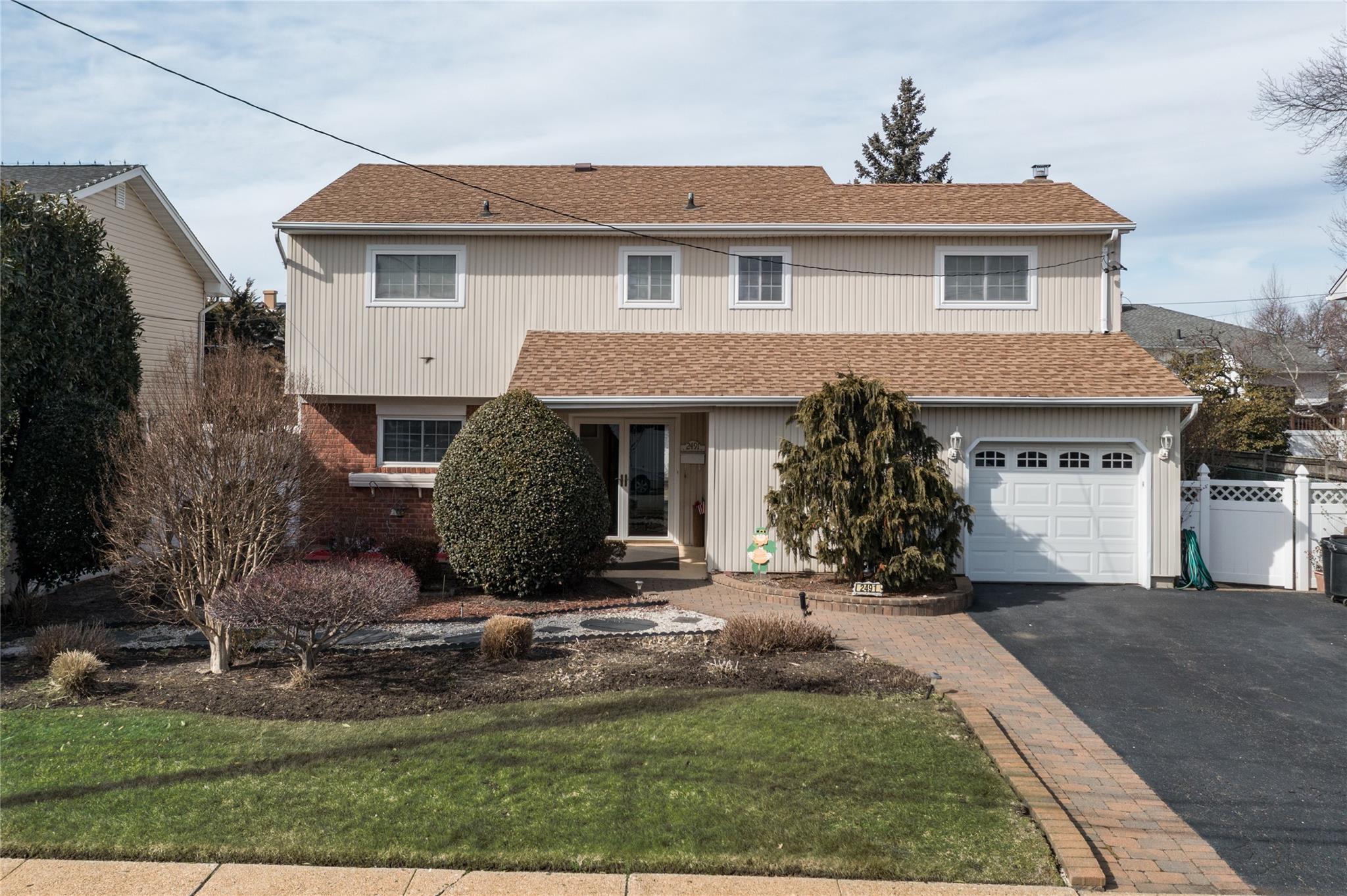 2491 Malibu Road Bellmore, NY 11710 - Photo 1 of 1 Traditional home featuring driveway, brick siding, a shingled roof, fence, and a front yard