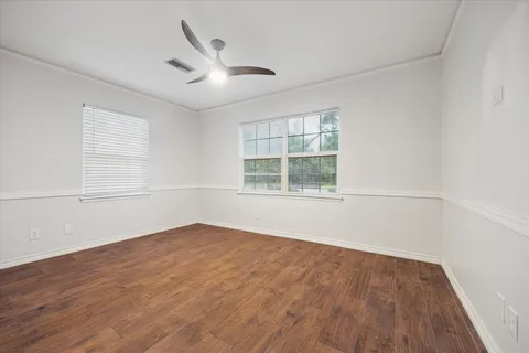 an empty room with wooden floor ceiling fan and windows