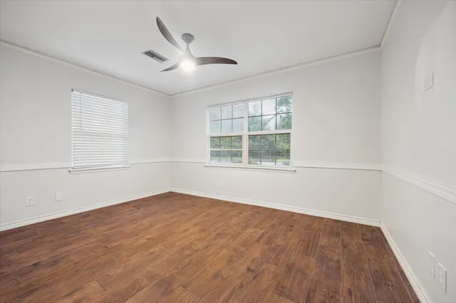 an empty room with wooden floor ceiling fan and windows