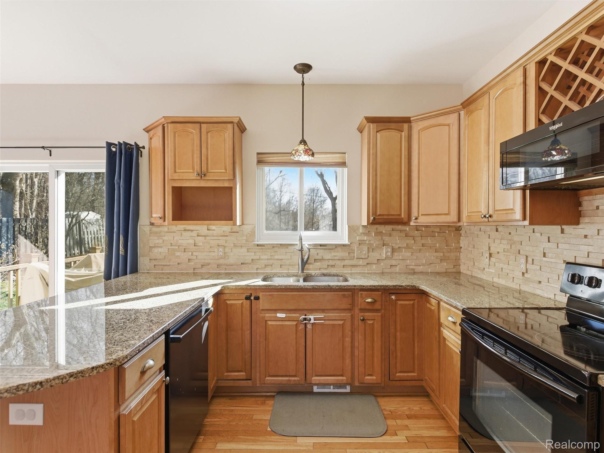 7640 Clintonville Road Clarkston, MI 48348 - Photo 9 of 27 Kitchen featuring black appliances, a peninsula, decorative backsplash, light stone countertops, and light wood-style floors