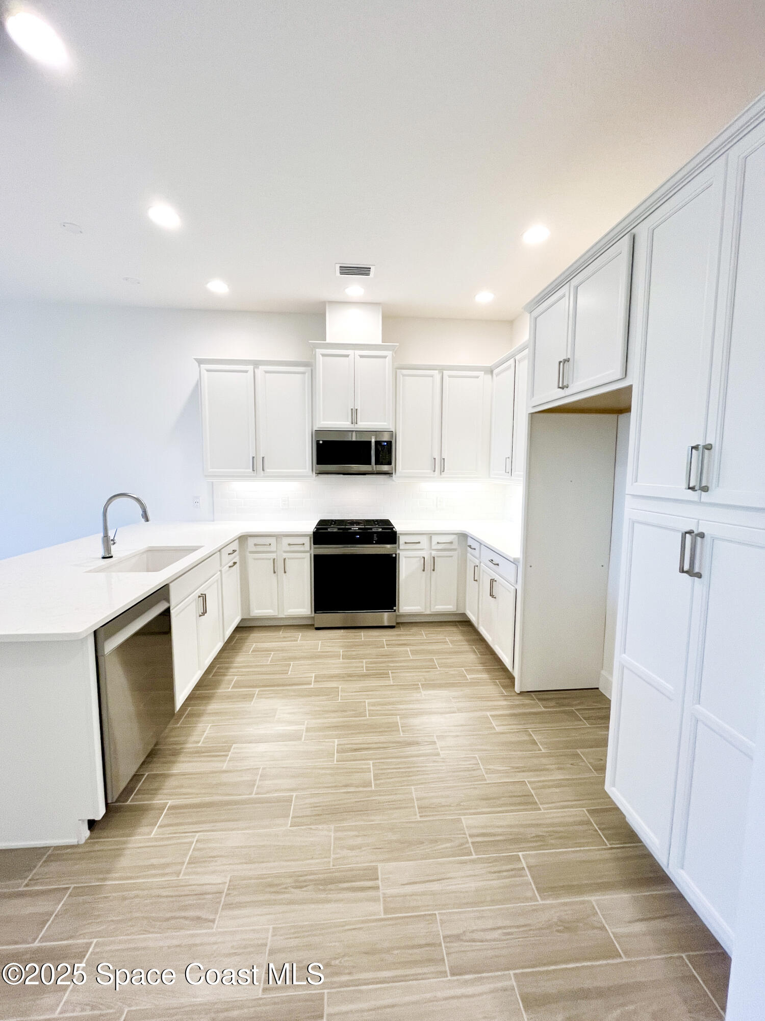 7707 Cache Crk Lane Melbourne, FL 32940 - Photo 6 of 18 a large white kitchen with white cabinets and wooden floor