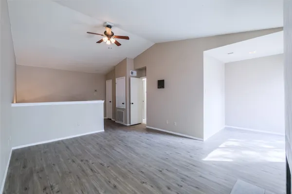 a view of an empty room with wooden floor and a ceiling fan