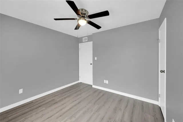an empty room with wooden floor ceiling fan and window