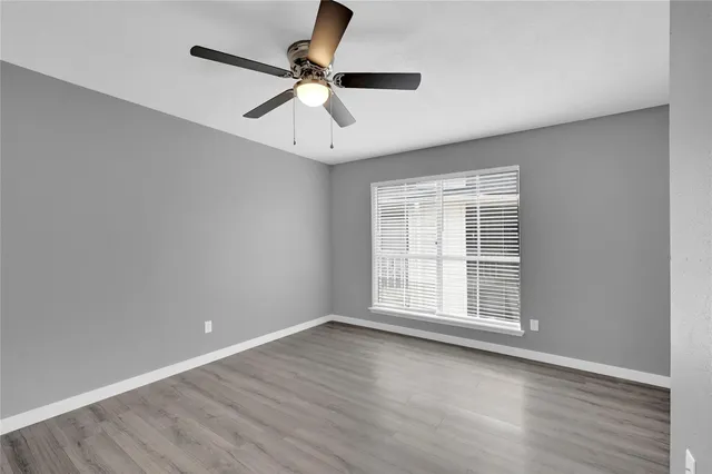 an empty room with wooden floor fan and windows