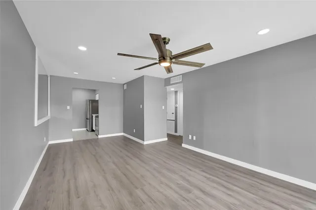 a view of an empty room with wooden floor and a ceiling fan