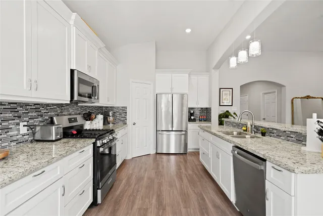 a kitchen with stainless steel appliances granite countertop wooden cabinets a sink dishwasher a stove and a refrigerator