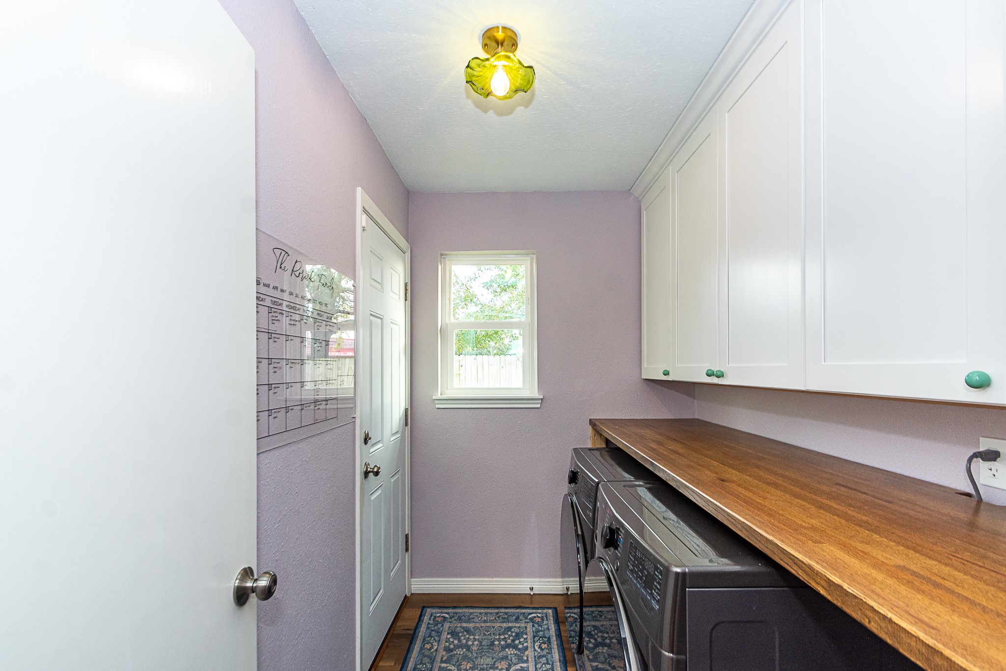 4830 Lost Oak Drive Spring, TX 77388 - Photo 13 of 41 This photo shows the functional laundry room with a washer and dryer, white cabinets, and a wooden countertop. It features a lavender wall, a window providing natural light, and a ceiling light fixture.