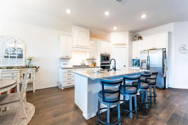 a kitchen with stainless steel appliances kitchen island granite countertop a dining table chairs and white cabinets