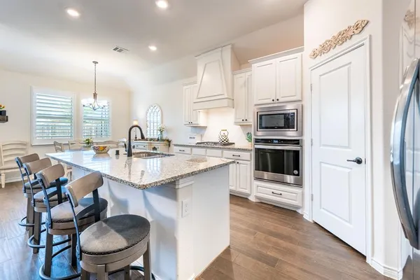 a kitchen with stainless steel appliances a sink a stove a refrigerator cabinets and a dining table with wooden floor