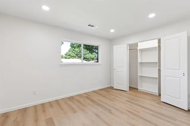 an empty room with wooden floor closet and windows