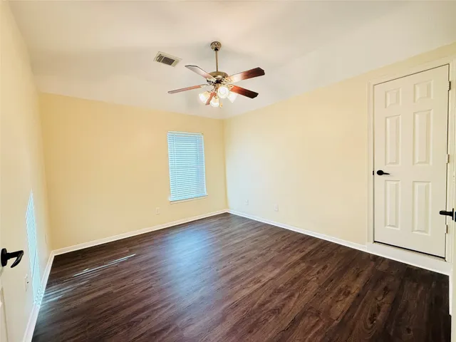 an empty room with wooden floor fan and windows