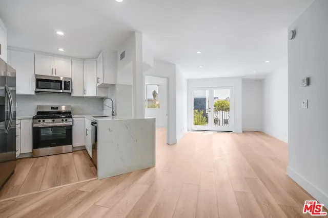 a kitchen with stainless steel appliances a stove top oven a sink a refrigerator white cabinets and wooden floor