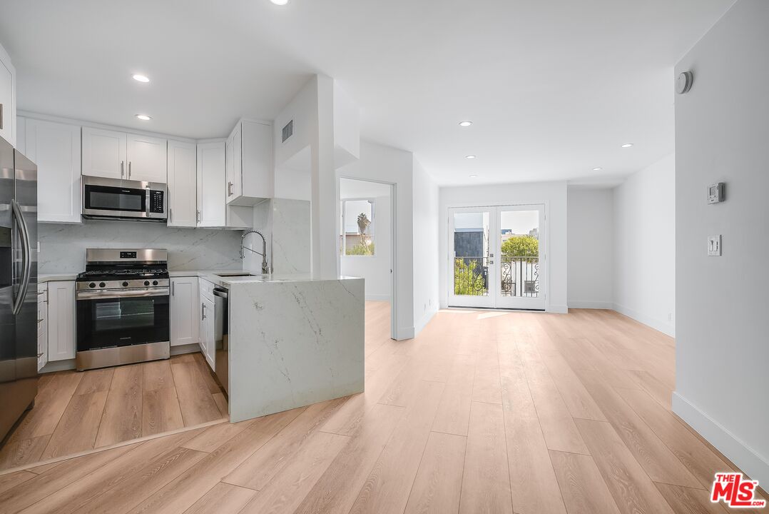11675 Darlington Avenue, Unit 301 Los Angeles, CA 90049 - Photo 5 of 16 a kitchen with stainless steel appliances a stove top oven a sink a refrigerator white cabinets and wooden floor