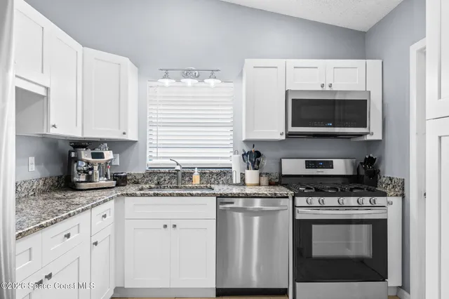 a kitchen with granite countertop white cabinets white stainless steel appliances and a sink