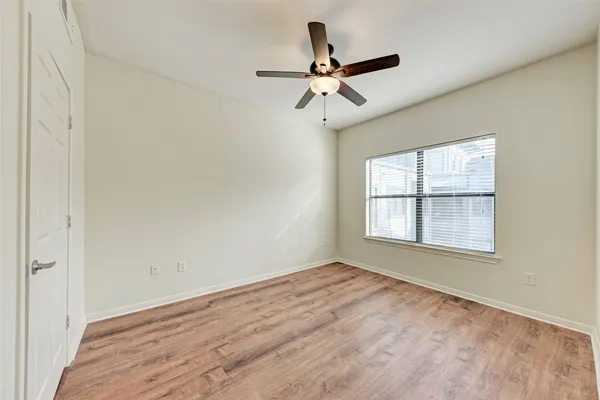 an empty room with wooden floor fan and windows