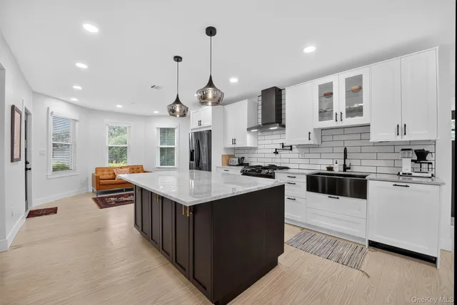 a kitchen with stainless steel appliances kitchen island granite countertop a stove top oven a sink dishwasher a refrigerator and white cabinets with wooden floor