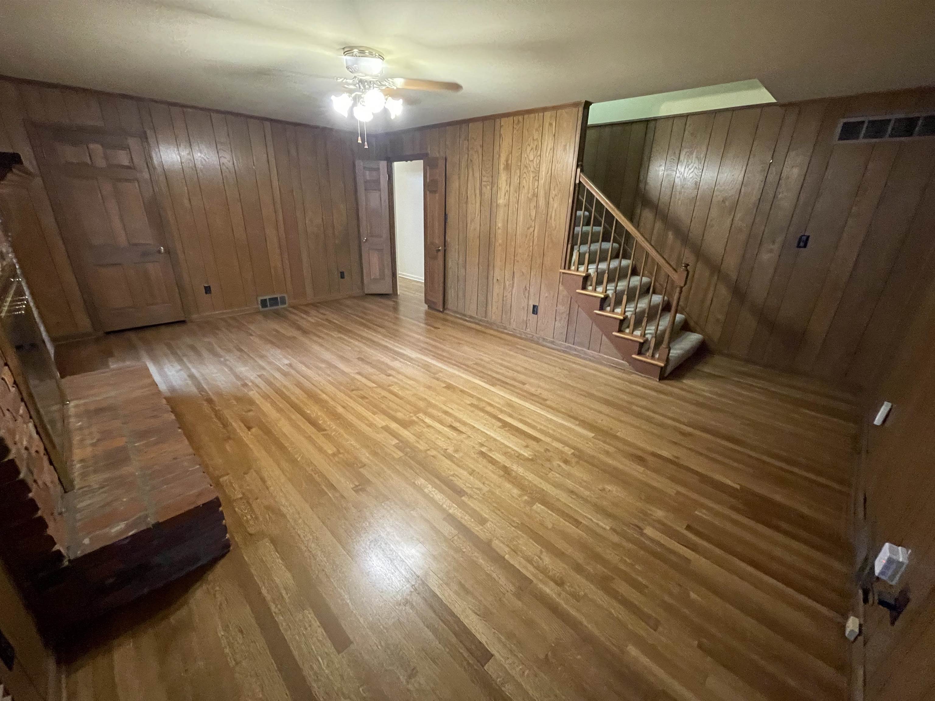 379 McElroy Road Memphis, TN 38120 - Photo 17 of 19 Unfurnished living room featuring stairway, light wood finished floors, a ceiling fan, and wood walls
