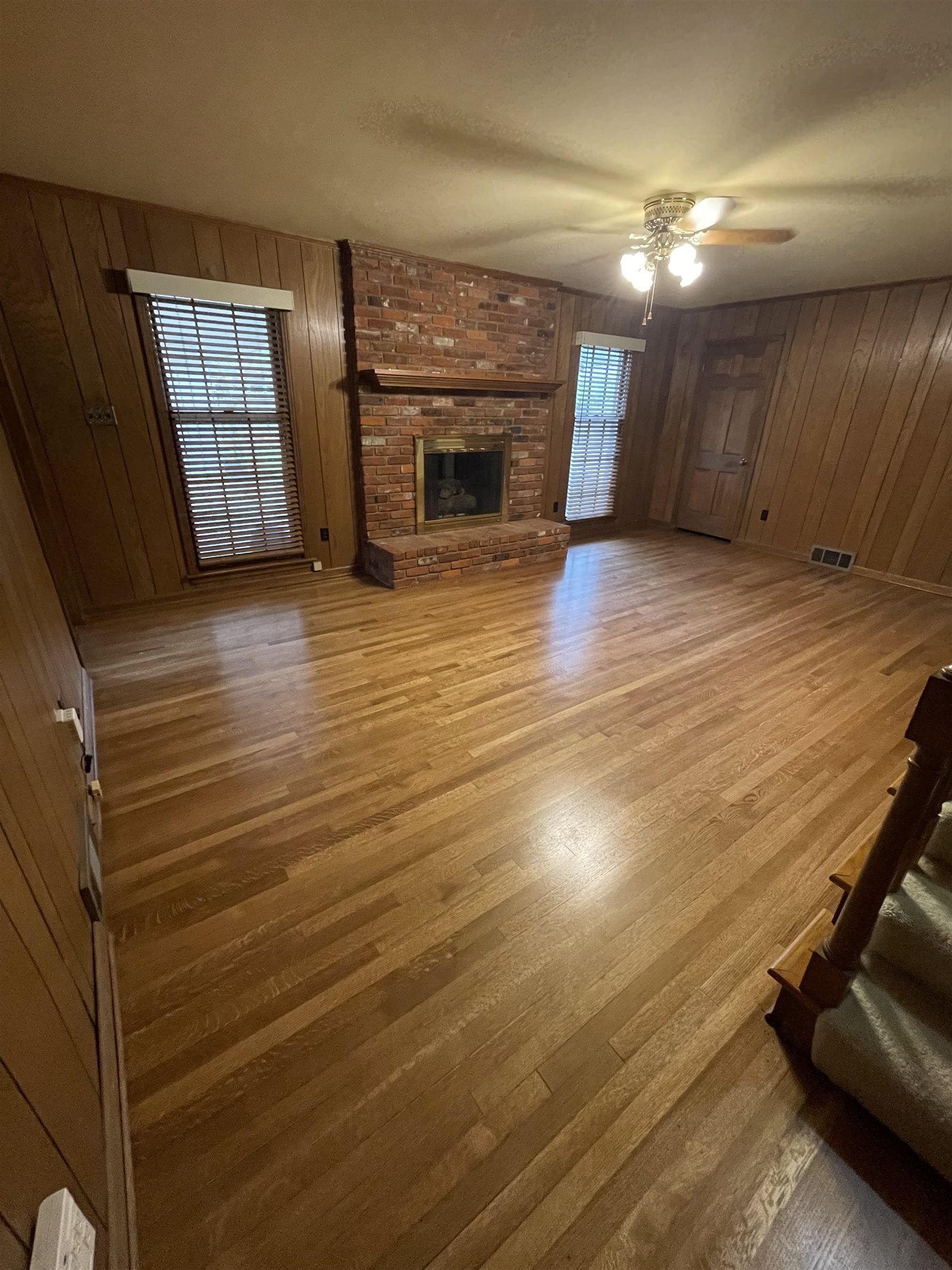 379 McElroy Road Memphis, TN 38120 - Photo 9 of 19 Unfurnished living room with wood walls, healthy amount of natural light, light wood-type flooring, a fireplace, and a ceiling fan