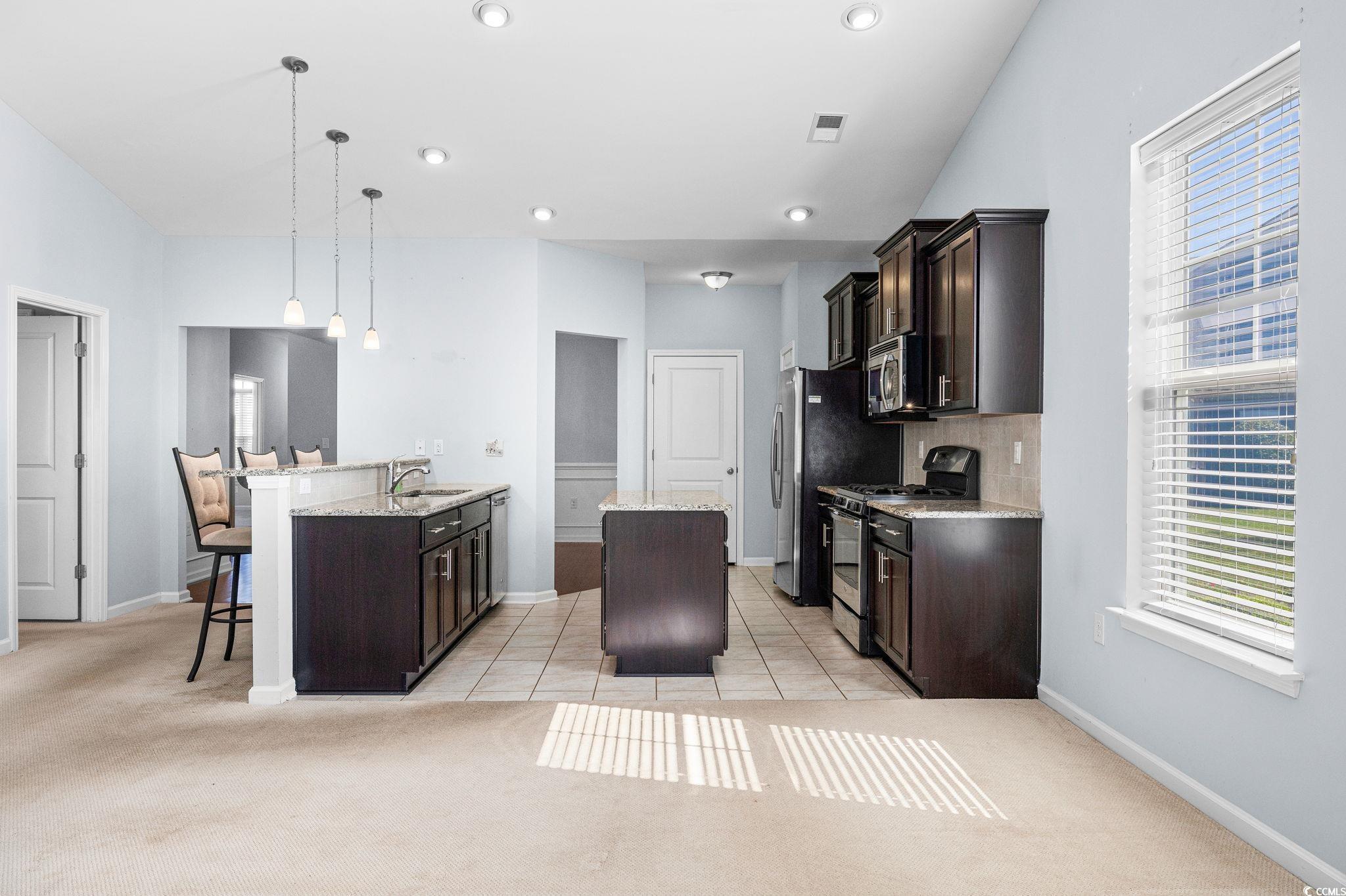 817 Arezzo Way, Unit 1001 Myrtle Beach, SC 29579 - Photo 16 of 40 Kitchen with dark brown cabinetry, light colored carpet, a center island, appliances with stainless steel finishes, and pendant lighting