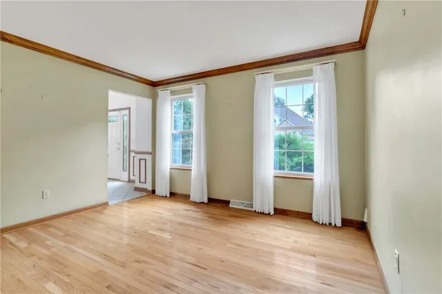 an empty room with wooden floor and windows with curtains