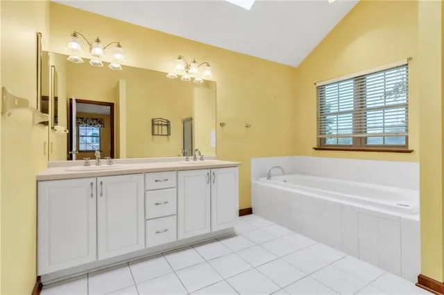 a spacious bathroom with a double vanity sink a mirror a bathtub and next to a window