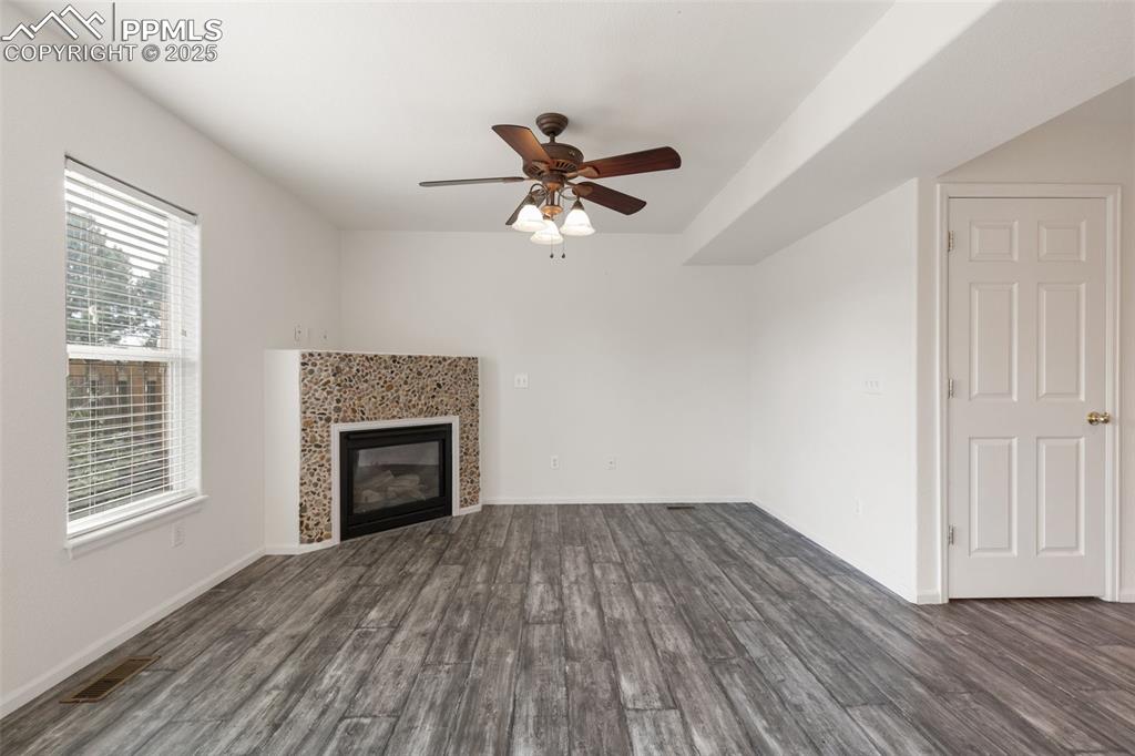 5679 Sunshade Point Colorado Springs, CO 80923 - Photo 3 of 30 an empty room with wooden floor a fireplace a ceiling fan and windows
