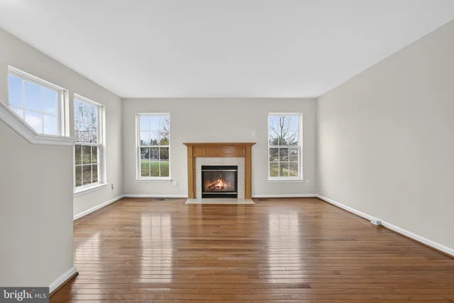 a view of an empty room with wooden floor fireplace and a window