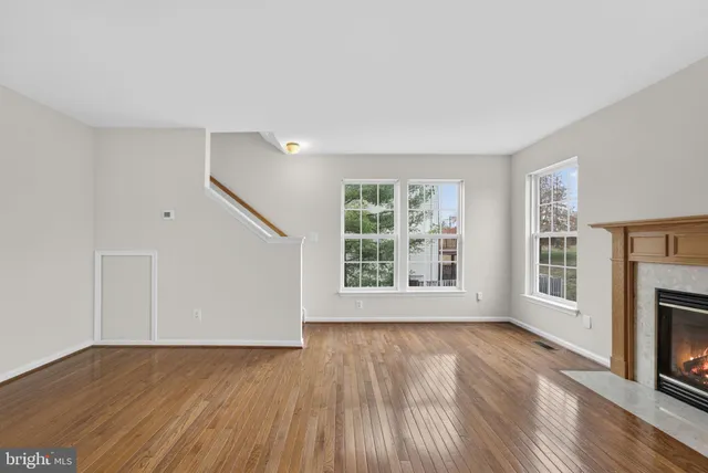 an empty room with wooden floor fireplace and windows