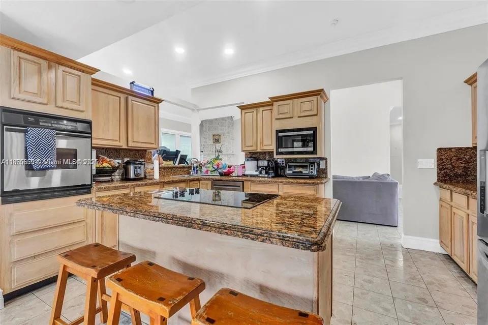 19905 Southwest 135th Avenue Miami, FL 33177 - Photo 8 of 34 a kitchen with stainless steel appliances granite countertop a stove top oven a sink a dining table and chairs with white cabinets