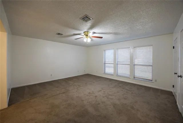 an empty room with chandelier fan and windows