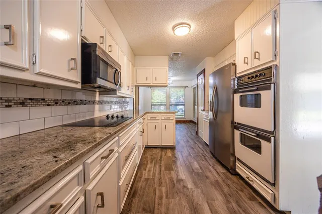 a kitchen with stainless steel appliances granite countertop a refrigerator a stove and a sink with wooden floor