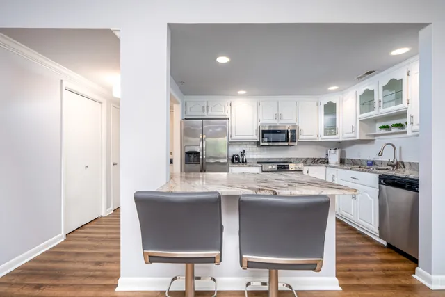 a kitchen with stainless steel appliances granite countertop a stove top oven a sink dishwasher and white cabinets with wooden floor