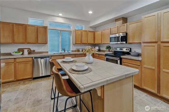 a kitchen with stainless steel appliances granite countertop a sink a stove a refrigerator a center island and chairs