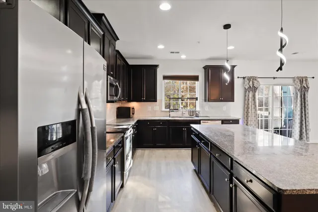 a kitchen with stainless steel appliances granite countertop a refrigerator a sink dishwasher a stove and a dining table with wooden floor