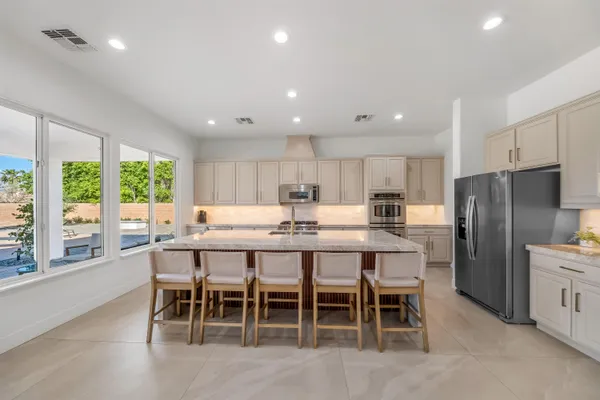 a large white kitchen with stainless steel appliances granite countertop a stove a sink a refrigerator and white cabinets