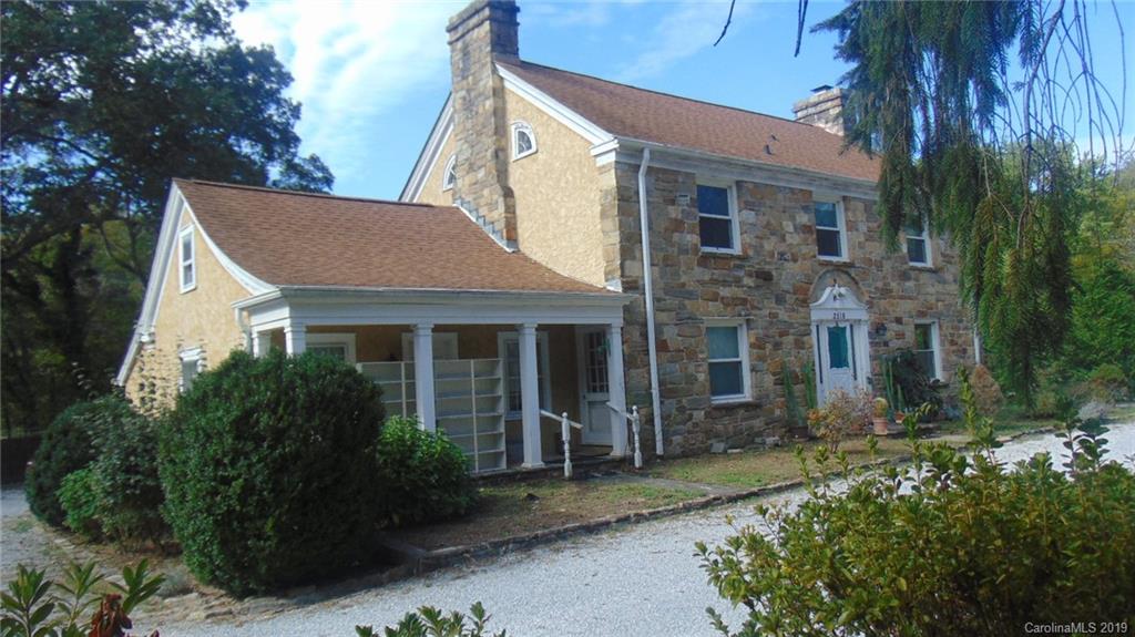 a view of a house with brick walls and a yard with plants and large tree