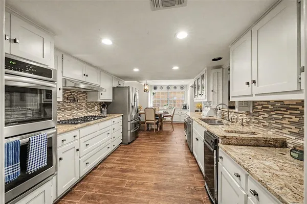 a large kitchen with stainless steel appliances granite countertop a stove top oven a sink dishwasher and a refrigerator