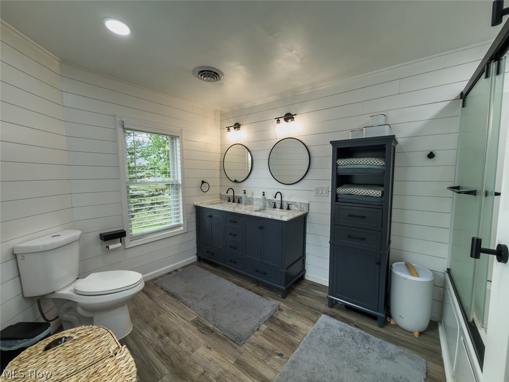 13429 West Calla Road Salem, OH 44460 - Photo 17 of 27 Bathroom featuring white shiplap walls, a dual vanity with a gray cabinet and stone-finish countertop, two round black-framed mirrors, and wood-finish flooring