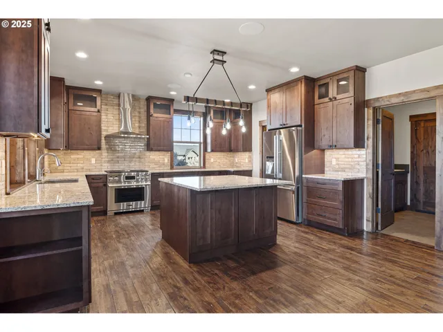 a kitchen with stainless steel appliances granite countertop a refrigerator a sink dishwasher a stove and a dining table with wooden floor