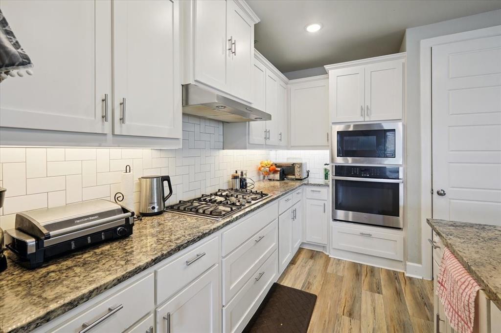 345 Greenbriar Road Little Elm, TX 75068 - Photo 9 of 20 Kitchen featuring white cabinets, appliances with stainless steel finishes, backsplash, light wood finished floors, and light stone countertops