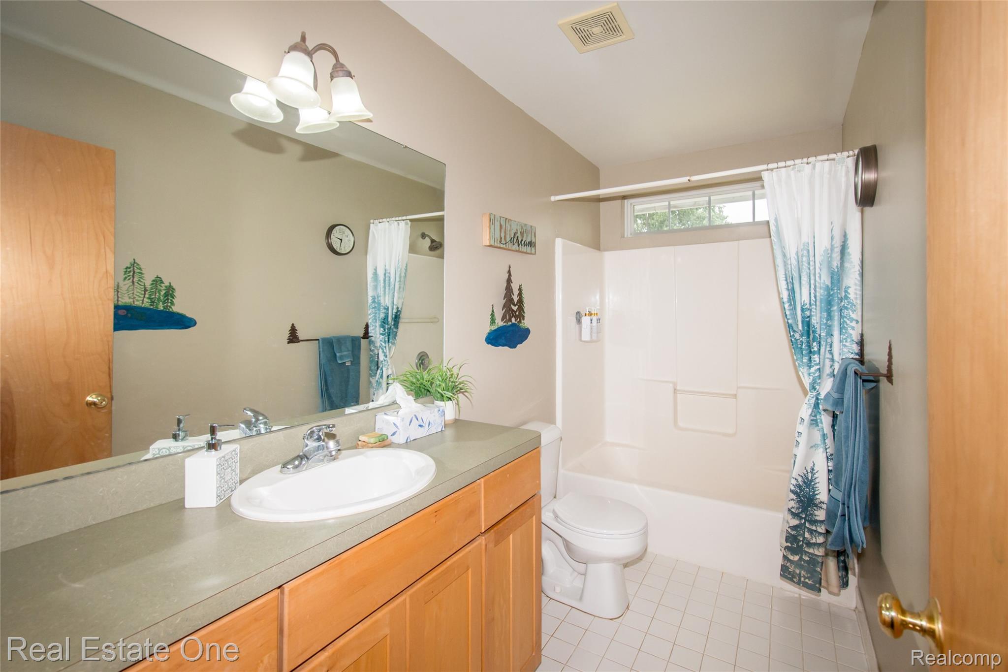 145 Stockbridge Road South Webberville, MI 48892 - Photo 23 of 35 Bathroom featuring a vanity with an integrated sink and light wood cabinetry, a large wall-mounted mirror, a tub/shower combination with a transom window, and white tile flooring